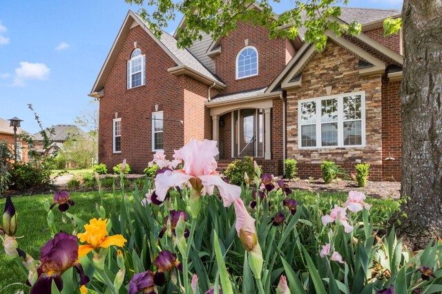 view of front of home with roof with shingles, brick siding, and stone siding
