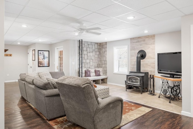 living area with baseboards, a paneled ceiling, ceiling fan, and a wood stove