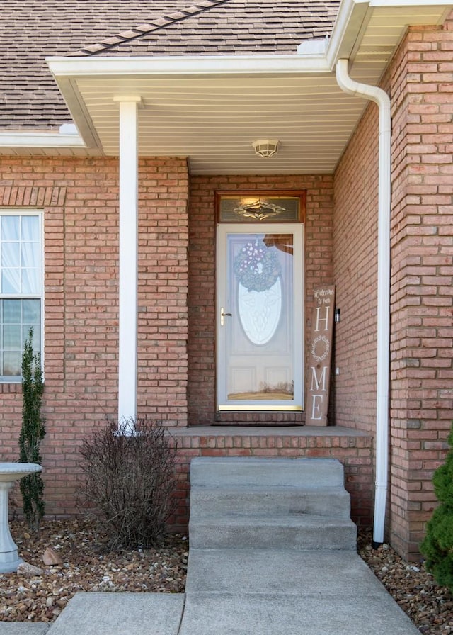 doorway to property featuring brick siding and a shingled roof