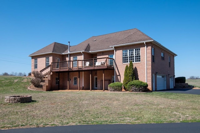 rear view of property with a deck, driveway, a yard, a fire pit, and a garage