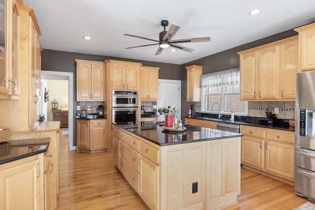 kitchen with light brown cabinets, dark countertops, light wood-style floors, appliances with stainless steel finishes, and ceiling fan