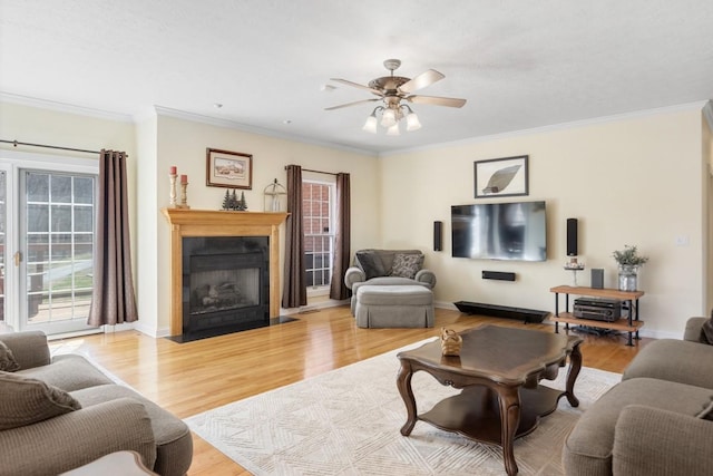 living area with a fireplace with flush hearth, crown molding, a ceiling fan, and light wood finished floors