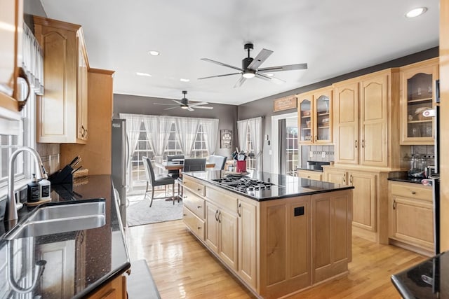 kitchen with a kitchen island, a sink, glass insert cabinets, appliances with stainless steel finishes, and light wood-type flooring