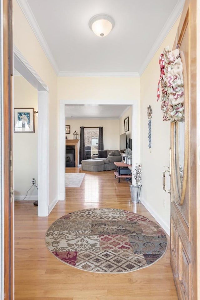 foyer entrance featuring baseboards, wood finished floors, a fireplace, and ornamental molding