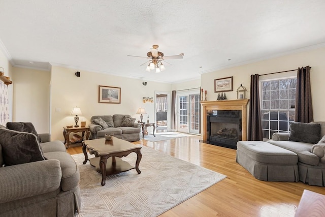 living area featuring light wood-style flooring, ornamental molding, a fireplace, and ceiling fan