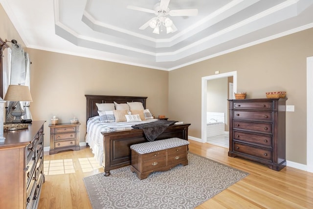 bedroom featuring a tray ceiling, ensuite bathroom, baseboards, and light wood finished floors