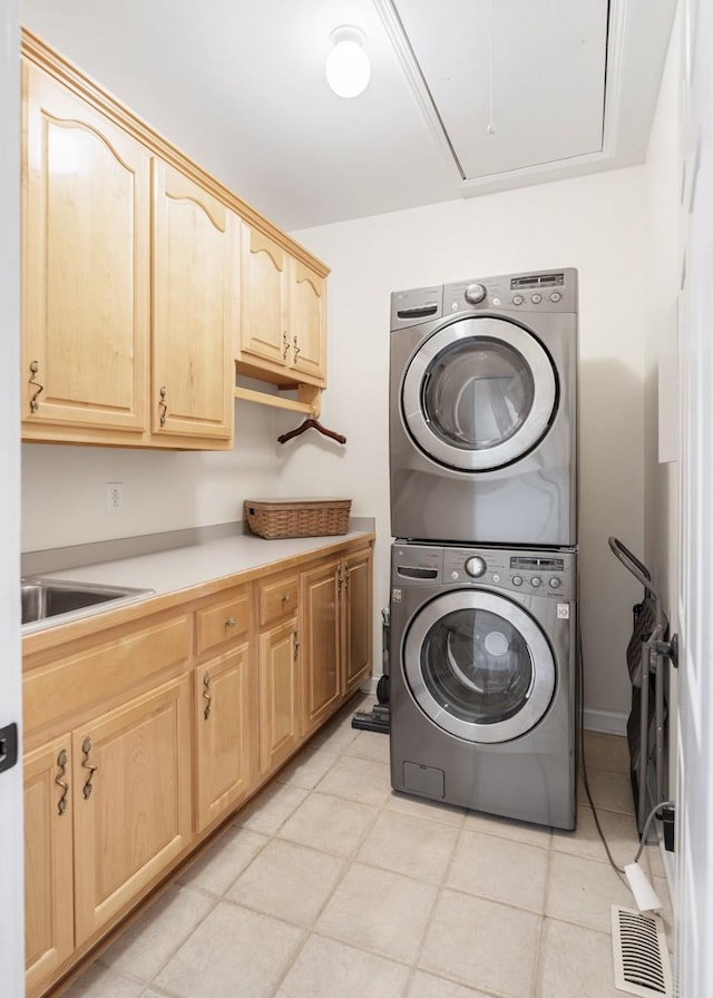 clothes washing area featuring visible vents, attic access, cabinet space, a sink, and stacked washer and dryer