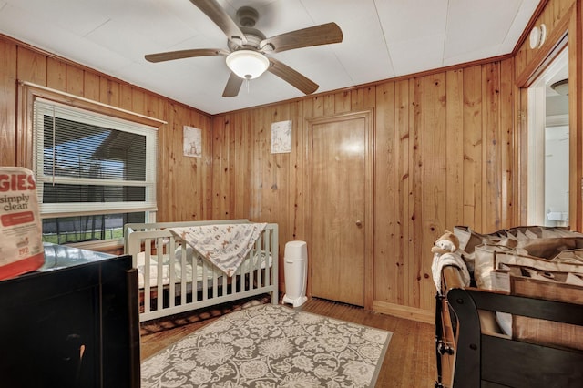 bedroom featuring a nursery area, a ceiling fan, wood finished floors, and wooden walls