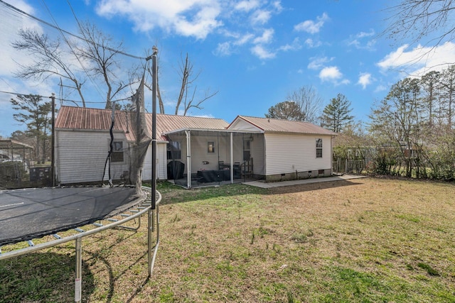 rear view of house with fence, a trampoline, driveway, a lawn, and metal roof