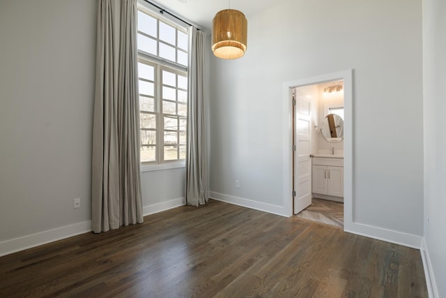 unfurnished bedroom with dark wood-type flooring, baseboards, and ensuite bathroom