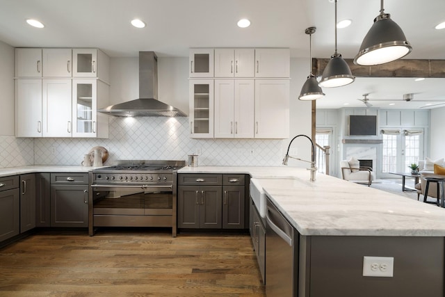 kitchen featuring a peninsula, a sink, stainless steel appliances, white cabinets, and wall chimney exhaust hood