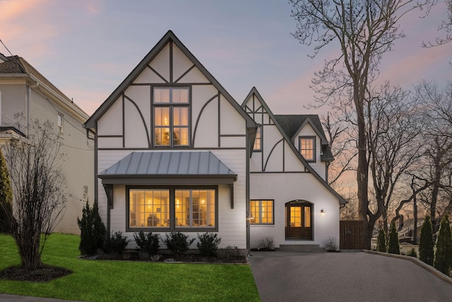 english style home with metal roof, stucco siding, a front lawn, and a standing seam roof