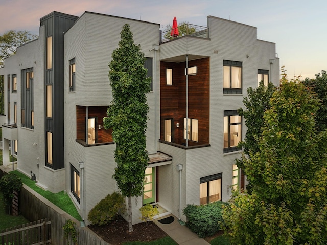 exterior space featuring brick siding, a balcony, and fence