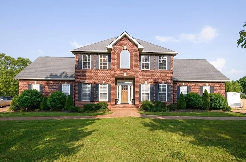 colonial home with a front lawn, brick siding, and roof with shingles