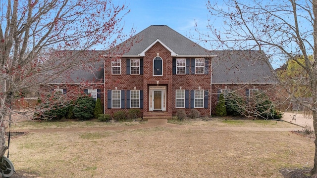 colonial-style house featuring a front lawn, brick siding, and a shingled roof