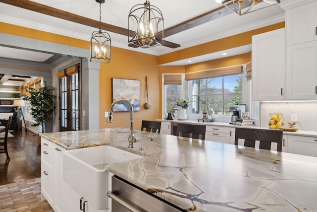 kitchen with a sink, an inviting chandelier, ornamental molding, and hanging light fixtures