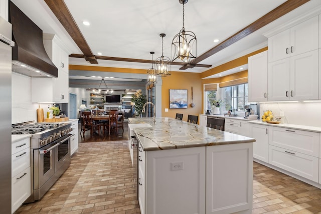 kitchen featuring double oven range, an island with sink, recessed lighting, wall chimney range hood, and a chandelier