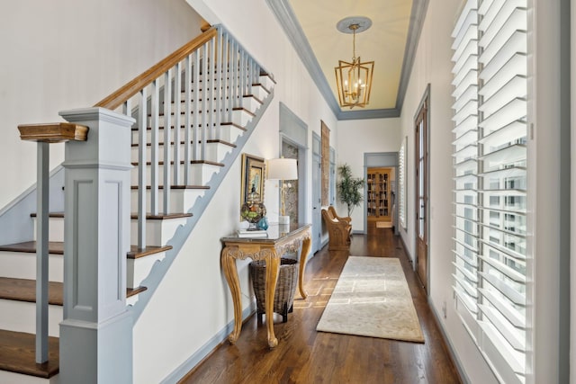 foyer entrance featuring dark wood finished floors, an inviting chandelier, ornamental molding, and stairs