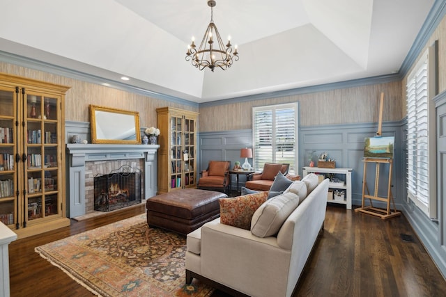 living area featuring an inviting chandelier, a tray ceiling, dark wood-style flooring, a brick fireplace, and a decorative wall