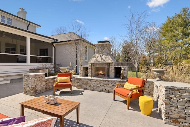 view of patio featuring a sunroom, a fire pit, an outdoor stone fireplace, and fence