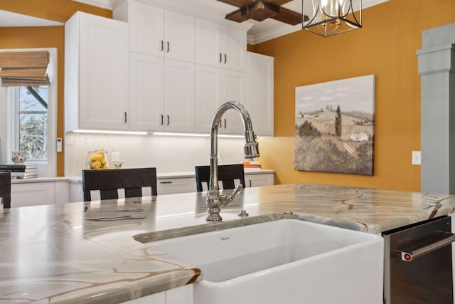 kitchen featuring light stone counters, a sink, white cabinets, crown molding, and a chandelier