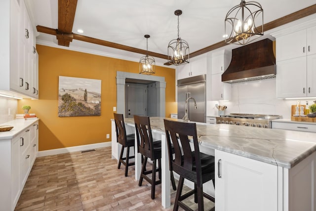 kitchen with baseboards, premium range hood, built in fridge, a notable chandelier, and backsplash