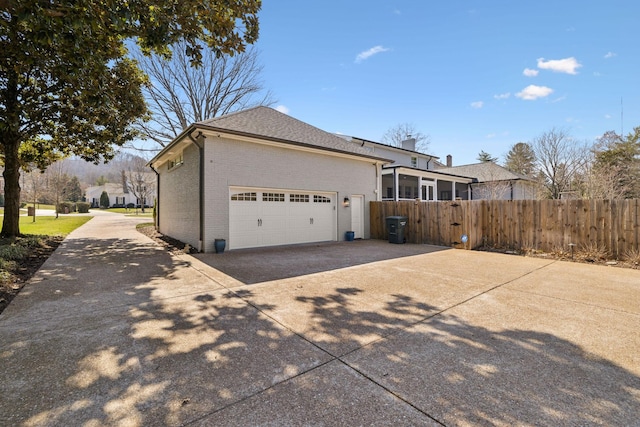 view of home's exterior featuring brick siding, an attached garage, a shingled roof, fence, and driveway