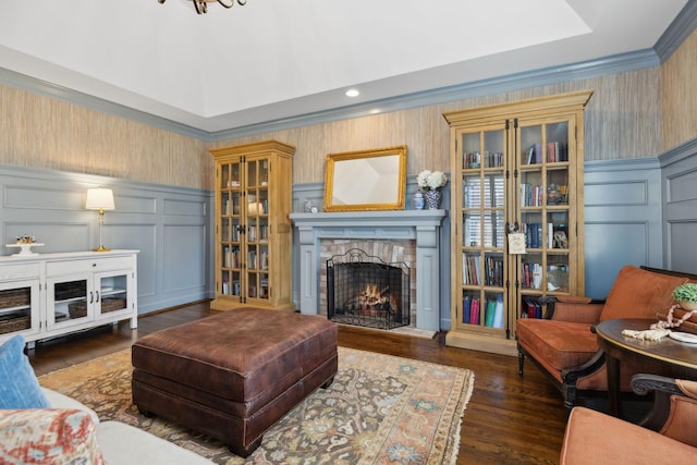 living room with a decorative wall, a warm lit fireplace, wainscoting, and wallpapered walls