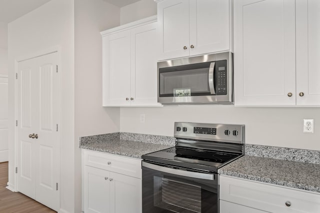 kitchen with light stone counters, appliances with stainless steel finishes, white cabinets, and light wood finished floors