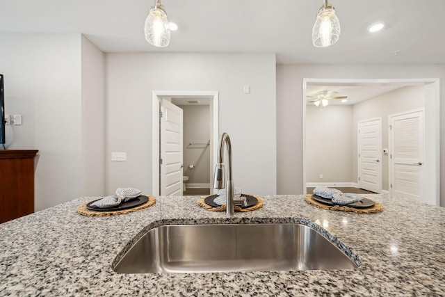 kitchen featuring a ceiling fan, pendant lighting, light stone countertops, and a sink