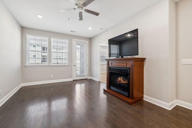 unfurnished living room featuring a glass covered fireplace, baseboards, dark wood-style floors, and ceiling fan