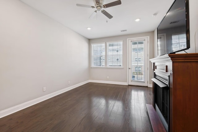 unfurnished living room with visible vents, a ceiling fan, a fireplace, baseboards, and dark wood-style flooring