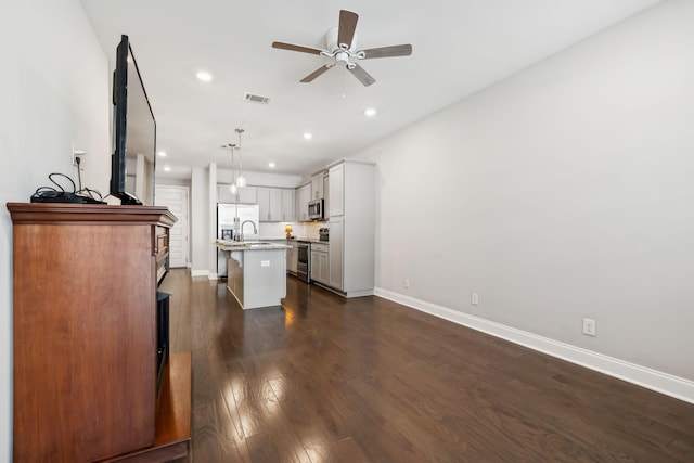 kitchen with a breakfast bar area, dark wood finished floors, ceiling fan, stainless steel appliances, and tasteful backsplash