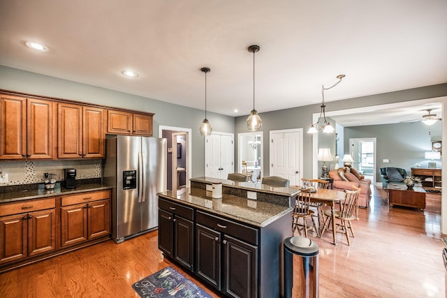 1013 Five Coves Trce, Gallatin, TN 37066 - kitchen featuring dark stone countertops, light wood finished floors, stainless steel fridge, pendant lighting, and brown cabinets