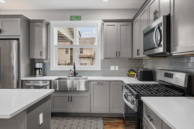 kitchen featuring backsplash, light countertops, gray cabinets, appliances with stainless steel finishes, and a sink