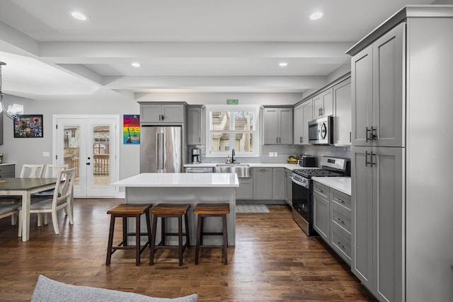 kitchen featuring dark wood-type flooring, gray cabinets, appliances with stainless steel finishes, a kitchen breakfast bar, and a sink