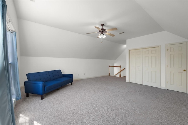 living area with visible vents, vaulted ceiling, an upstairs landing, carpet flooring, and a ceiling fan