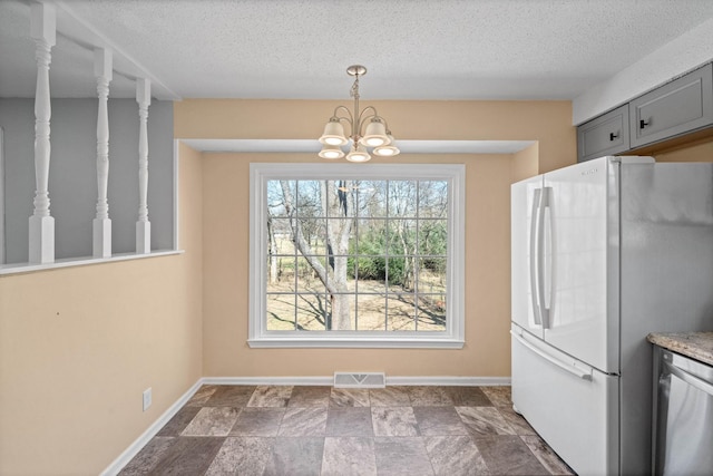 unfurnished dining area featuring an inviting chandelier, baseboards, visible vents, and a textured ceiling