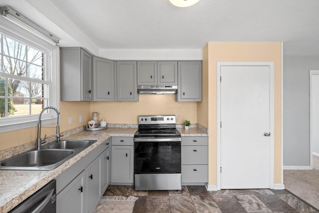 kitchen with gray cabinetry, under cabinet range hood, a sink, appliances with stainless steel finishes, and light countertops