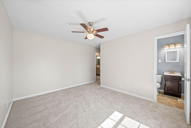 unfurnished bedroom featuring a ceiling fan, ensuite bathroom, a sink, baseboards, and light colored carpet