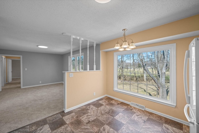 unfurnished dining area with baseboards, visible vents, an inviting chandelier, stone finish floor, and dark colored carpet