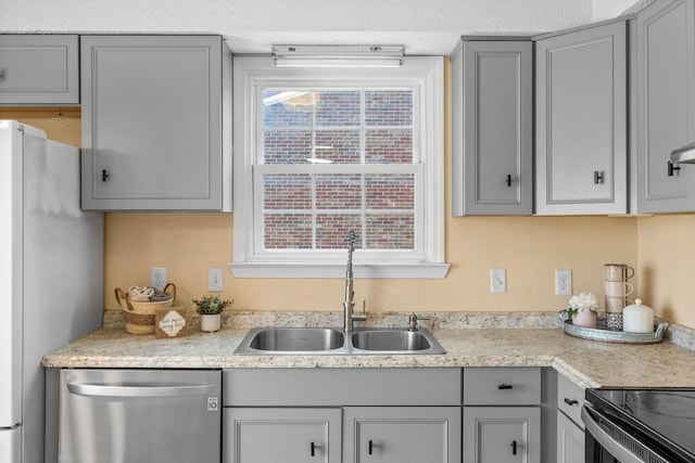 kitchen featuring light countertops, gray cabinets, stainless steel dishwasher, freestanding refrigerator, and a sink