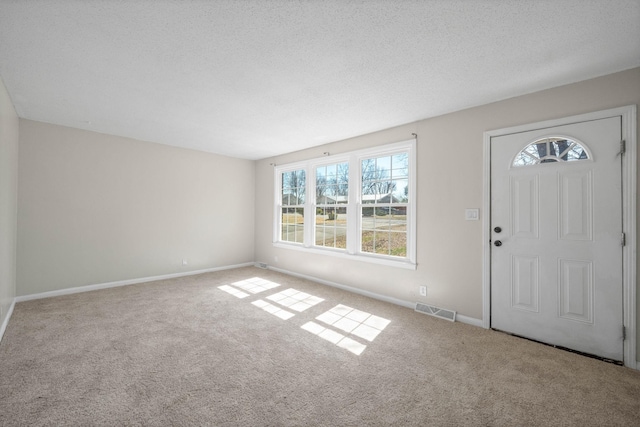 carpeted foyer featuring visible vents, a textured ceiling, and baseboards