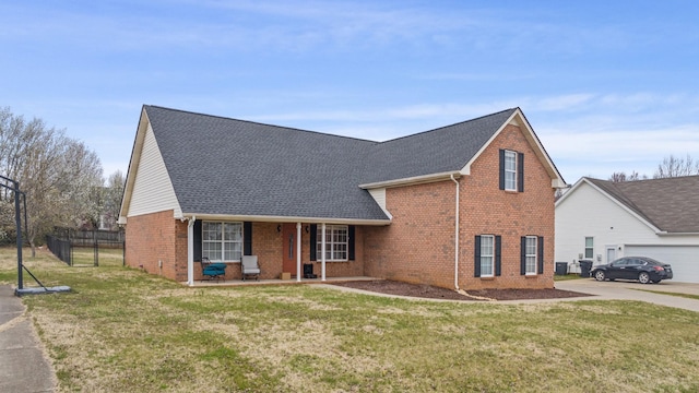 traditional-style home featuring fence, covered porch, a shingled roof, a front lawn, and brick siding