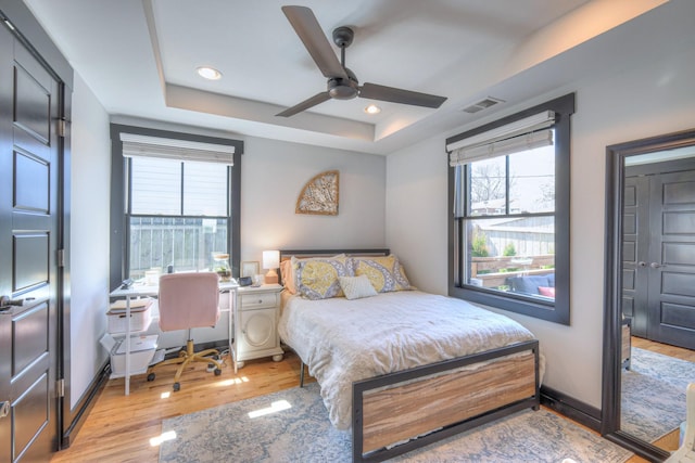 bedroom featuring baseboards, visible vents, light wood finished floors, recessed lighting, and a raised ceiling