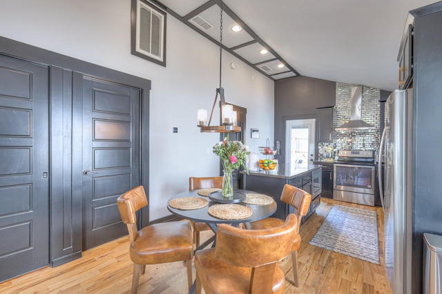 dining space featuring light wood-type flooring, visible vents, and high vaulted ceiling