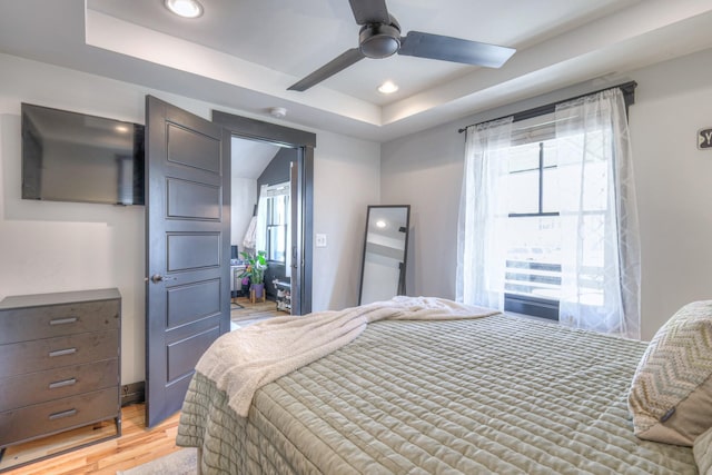 bedroom featuring recessed lighting, a tray ceiling, light wood-style flooring, and a ceiling fan