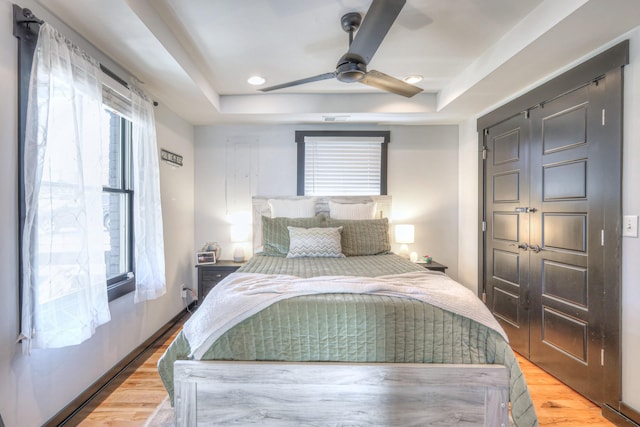 bedroom featuring recessed lighting, a raised ceiling, light wood-style flooring, and a ceiling fan