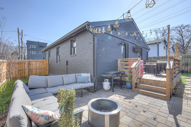 rear view of house with a wooden deck, brick siding, an outdoor living space with a fire pit, and a fenced backyard