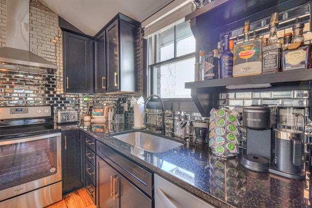 kitchen featuring dark stone countertops, lofted ceiling, stainless steel electric range, a sink, and wall chimney range hood